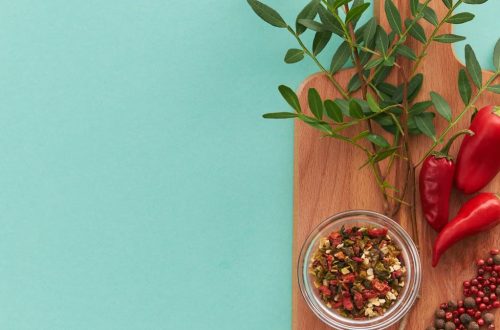Top view of peppers, spices, and green leaves on a wooden board with teal background, offering copy space.